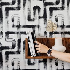 a person's hand on a book shelf next to a wallpaper with black and white squares