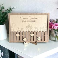 a mother's garden love grows here sign on a shelf with flowers in the background