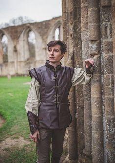 a young man dressed in medieval clothing leaning against a stone wall