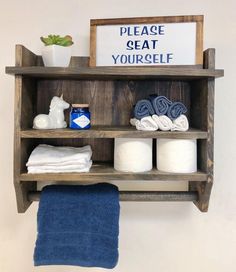 a wooden shelf with towels, toilet paper and other items on it that says please seat you're self