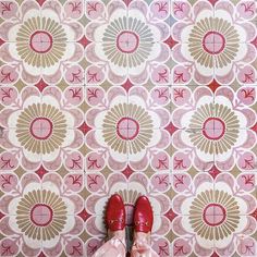 a pair of red shoes standing in front of a wall with pink and gold designs