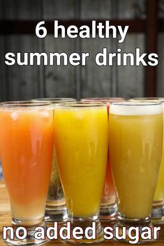 four glasses filled with different colored drinks on top of a wooden table next to each other