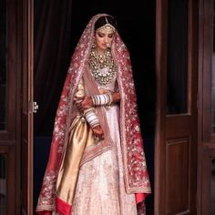 a woman in a red and gold bridal gown standing outside an open door with her hands on her hips