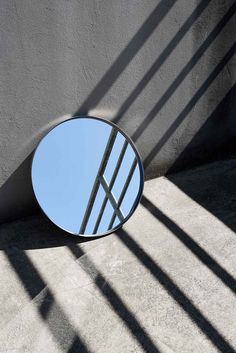 a round mirror sitting on the side of a wall next to a shadow filled floor