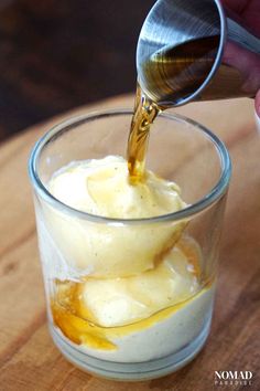 someone pouring sauce into a glass on top of a wooden table with food in it