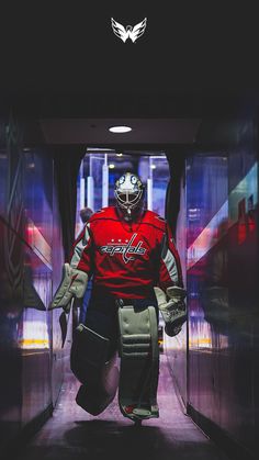 a hockey goalie is walking into the locker room with his helmet on and gloves in hand