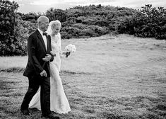 the bride and groom are walking through the field in black and white, holding each other's hands