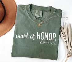 a t - shirt that says maid of honor on it next to a hat