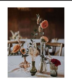 three vases filled with flowers sitting on top of a white tablecloth covered table