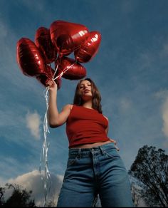 a woman holding red heart shaped balloons in the air