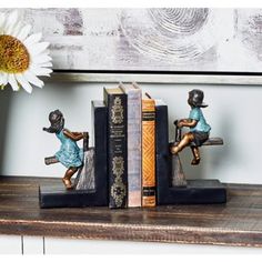 three little figurines are sitting on top of books and one is holding a flower