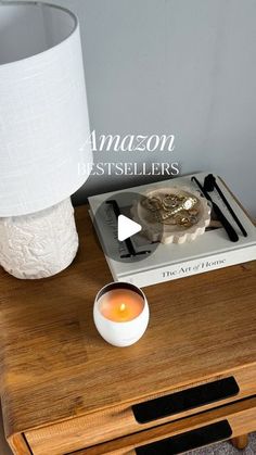 a wooden table topped with a white candle and a book next to a lamp shade