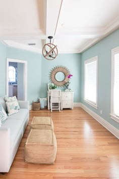 a living room with blue walls and wooden floors, white furniture and windows in the background