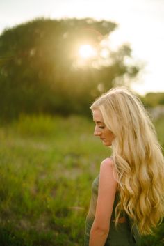 a woman with long blonde hair standing in the grass looking off into the distance at sunset