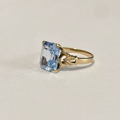 Beautiful 1940s era vintage 10k rosy yellow gold ring featuring a swiss blue topaz stone. The radiant blue topaz stone is radiant cut and secured by four prongs. The ring's shoulders are elegantly cinched with milgrain and repousse design details. Lovely piece of fine vintage jewelry, circa 1940! ERA - Circa 1940s / Retro METAL / MATERIAL - 10k gold, blue topaz MARKINGS / HISTORY - 10k SIZE / MEASUREMENTS - Size: 6 , Swiss Blue Topaz stone: approximately 10 x 8 mm, Weight: 2.15 grams, Shank: Tap Classic Light Blue Topaz Ring For Formal Occasions, Vintage Blue Topaz Ring With Prong Setting, Classic Light Blue Topaz Ring For Anniversary, Vintage Blue Topaz Ring For Formal Occasions, Vintage Yellow Gold Rings With Blue Topaz, Vintage Yellow Gold Blue Topaz Rings, Classic Topaz Birthstone Ring, Classic Light Blue Topaz Ring, Vintage Blue Topaz Ring In 14k Gold