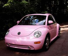 a pink car is parked on the side of the road in front of some trees