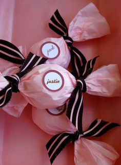 three candy wrapped in pink and black ribbons with name tags on them, sitting next to each other