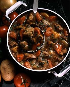 a pot filled with meat and vegetables on top of a table next to some potatoes