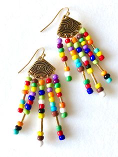 "Trendy multicolored seed bead chandelier earrings with golden tribal accents. Colorful tiny seed beads wire wrapped on gold plated pewter tribal fan shaped components made in USA. Lots of movement. Total drop is 2 5/8\"." Multicolor Beaded Earrings With Gold Beads As Gift, Multicolor Round Beads Earrings With Gold Beads, Traditional Multicolor Beaded Earrings With Gold Beads, Multicolor Gold Beads Dangle Earrings, Multicolor Dangle Earrings With Gold Beads, Multicolor Drop Earrings With Gold Beads, Multicolor Dangling Beads Chandelier Earrings Gift, Multicolor Dangling Beads Chandelier Earrings For Gifts, Bohemian Rainbow Earrings With Dangling Beads