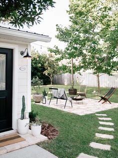 a patio with chairs and plants in the grass next to a door that leads into a backyard