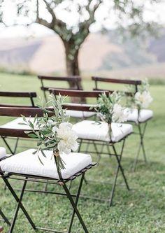 four folding chairs with flowers on them are sitting in the grass near a large tree