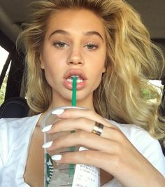 a woman with blonde hair drinking from a green straw in the back seat of a car