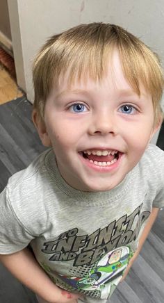 a young boy with blue eyes and blonde hair smiles at the camera while holding a toothbrush in his hand