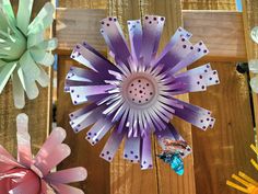 three different colored paper flowers on a wooden surface