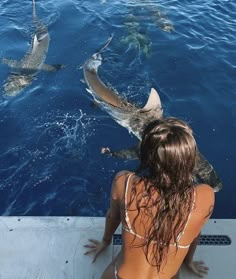 a woman sitting on the side of a boat looking at some sharks in the water