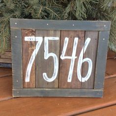 a wooden sign sitting on top of a table next to a pine tree and potted plant