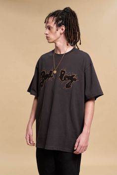 a young man with dreadlocks standing in front of a beige background wearing a black shirt