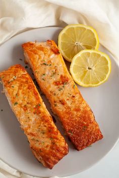 two salmon fillets on a white plate with lemons