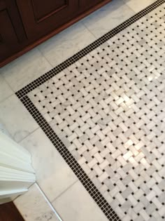 a white and black tiled floor in a bathroom with dark wood cabinets on the side