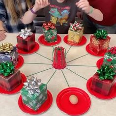 a group of people sitting around a table with christmas presents on red plates and wrapped gifts