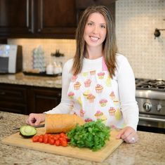 a woman standing in front of a cutting board with vegetables and a loaf of bread