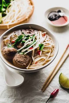 a bowl filled with meatballs and noodles next to chopsticks on a table