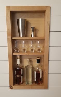 a shelf filled with bottles and glasses on top of a white wall next to a metal cup