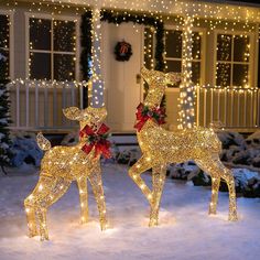 two lighted deer statues in front of a house with christmas lights on it's side