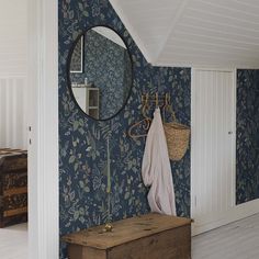 a room with blue wallpaper and a wooden bench in front of a round mirror