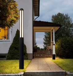 two lights that are on the side of a house near some grass and bushes in front of a white building