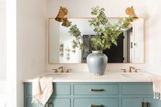 a bathroom with two sinks and a large mirror over it's countertop, along with a plant in a vase on the sink