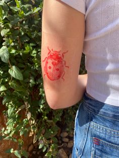 a ladybug tattoo on the arm of a woman's left arm, with red ink