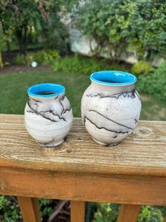 two white and blue vases sitting on top of a wooden table next to each other