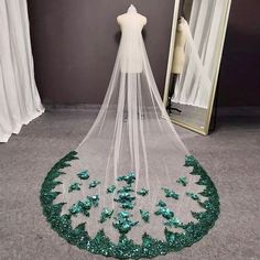 a wedding veil with green sequins on the bottom is displayed in front of a mirror