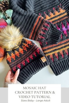 a woman's hand holding a knitted hat next to two sweaters and a ball of yarn