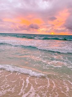 the sun is setting over the ocean with waves coming in to shore and pink clouds