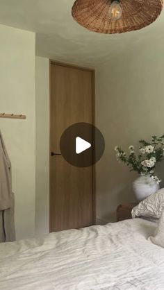 a bed with white sheets and pillows next to a wooden door in a room that has a wicker ceiling fan