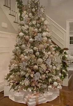 a decorated christmas tree in the middle of a living room with stairs and banisters