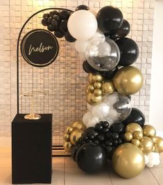 black, white and gold balloons are stacked on top of each other in front of a sign that reads nelson