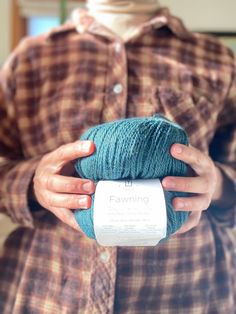 a woman holding a ball of yarn in her hands and wearing a flannel shirt